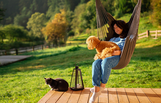 Woman with dog and cat resting on the hanging chair on the terrace mountain chalet. On the mountain background.