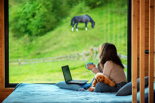 Woman sitting on the bed and looks outside the window seeing mountain.