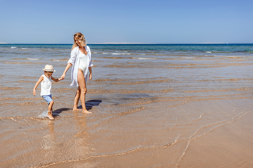 Photo of carefree mother and son holding hands while walking on the beach. with Copy space.