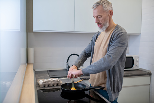 Breakfast. A gray-haired man cooking omlette in the kitchen