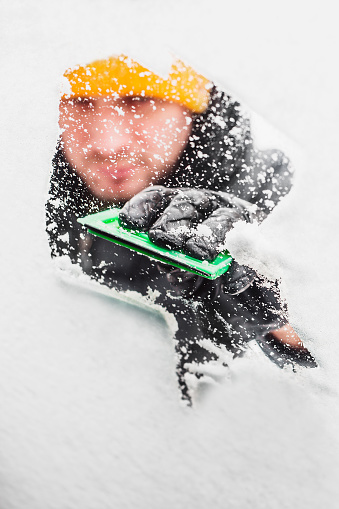 View from under the glass covered with snow of the car from the inside on the driver with a scraper