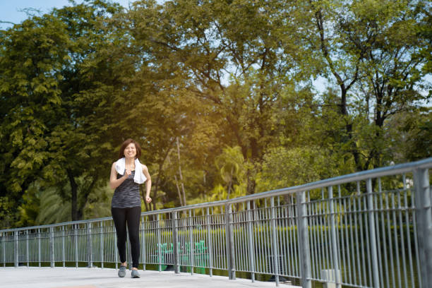 Beautiful Middle-aged Asian woman running in sportswear is smiling happy in park morning. Exercise make body healthy. Workout is health care Good stock photo