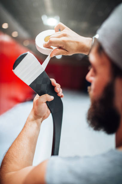 Bearded male ice hockey player wraps tape around hook hockey sticks to protect Bearded male ice hockey player wraps tape around hook hockey sticks to protect against impact and damage - preparing for a hockey game checking ice hockey stock pictures, royalty-free photos & images