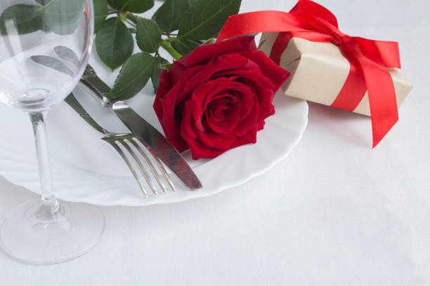 istock Festive table setting with red rose and gift box on the white tablecloth. Close-up. 1342468870