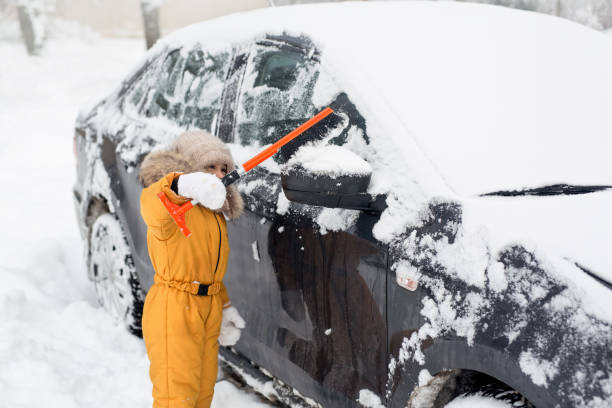 un piccolo bambino di cinque anni che spazzola via la neve dall'auto dopo la tempesta - snow car window ice scraper foto e immagini stock