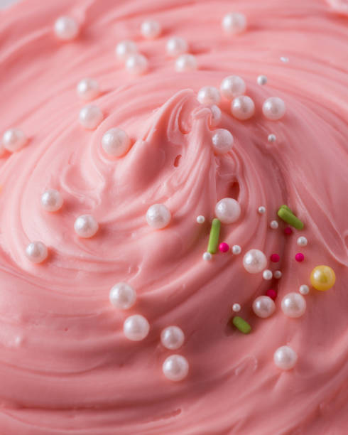 istock Pink icing frosting with small sprinkles close up texture 1342475037