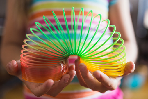 Close-up of a slinky toy in children's hands against the background of a colored strip T-shirt - selective focus on the toy