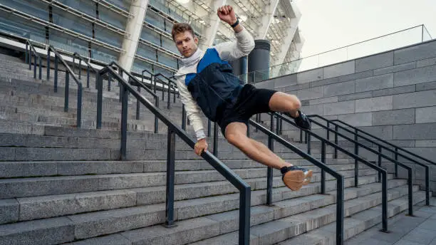 Full length portrait of sporty man jumps over the railing in the city. Sportsman running at daily outdoors training. Physical activity, motion and parkour concept