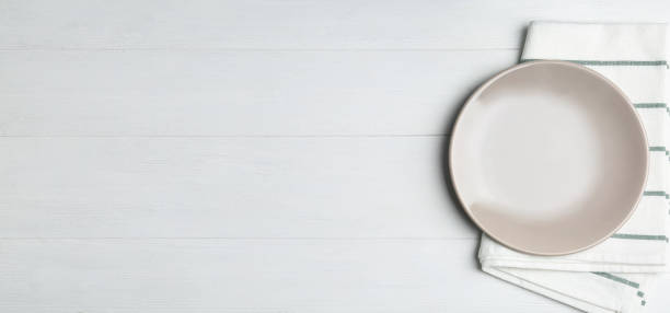 istock Empty grey plate and napkin on white wooden table, flat lay. Space for text 1342481610