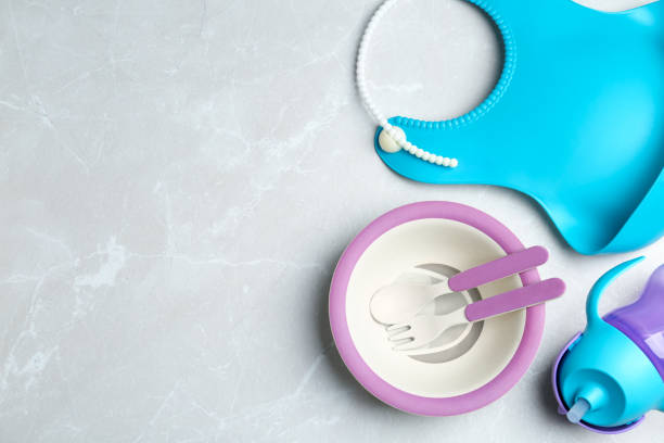istock Set of colorful plastic dishware and silicone bib on light grey marble table, flat lay with space for text. Serving baby food 1342481656
