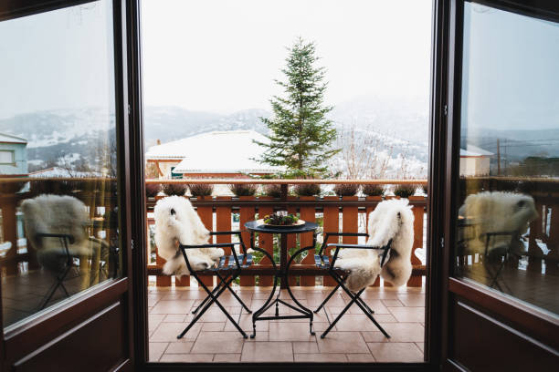 balcone invernale con tavolino, sedie accoglienti ricoperte di pelliccia bianca e splendida vista sulle montagne innevate. vacanze invernali - winter chalet snow residential structure foto e immagini stock