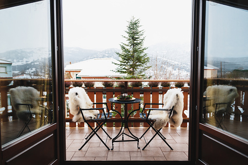 Winter balcony with coffee table, cozy chairs covered with white fur and splendid snow-covered mountains view. Winter vacation