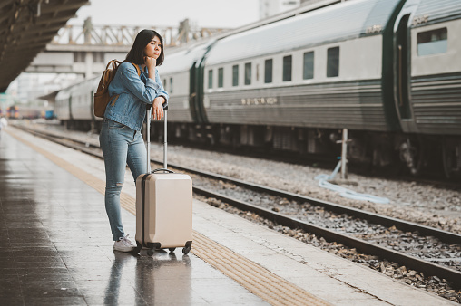 Asian woman traveler with luggage standing alone waiting for train at train station platform