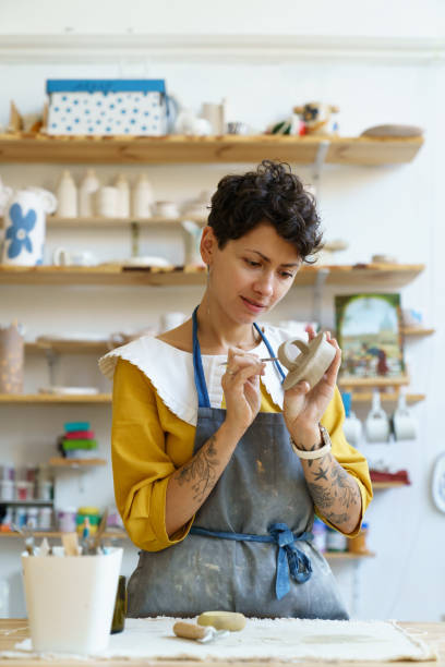 la ceramista artigiana femmina impegnata con il processo creativo usa strumenti per decorare l'argilla dello stampo e modellare le stoviglie - craft product foto e immagini stock