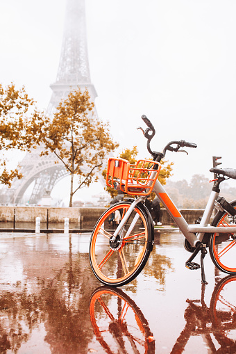 Orange bike in the rain on a wet stone street against the backdrop of the Eiffel Tower in Paris