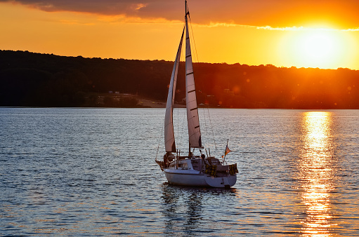 A small sailing ship sailing on a calm sea at the sunset