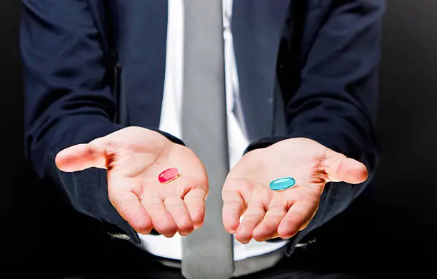 Photo of Male hands holding two gel pills One is red the other blue