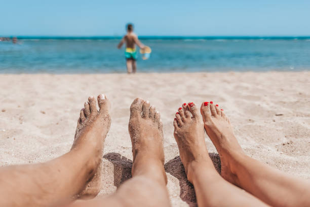 Sandy toes and feet of a couple enjoying a beach vacation while watching their kid playing in the sand.
