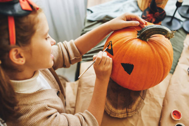 Little kid girl making Jack-o-lantern while preparing for Hallow