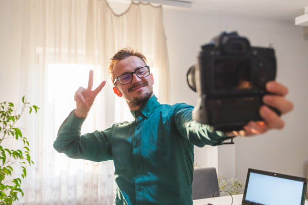 istock Young white male with glasses vlogging with a professional DSLR camera while doing a peace sign with his hand 1342502379