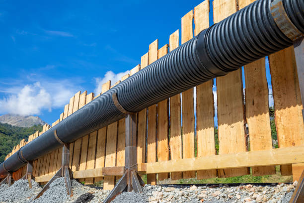 Temporary elevated sewer pipe supported by steel pedestals against wood fence in mountains stock photo
