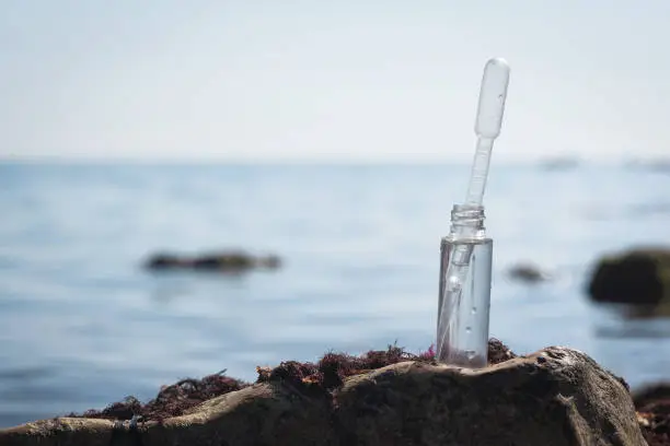 Sea water pollution concept. Sea water in the test tube on the stone close up.