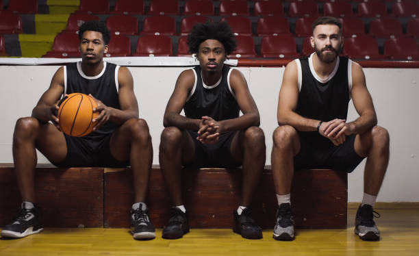 Three basketball players sitting on a bench watching the game stock photo