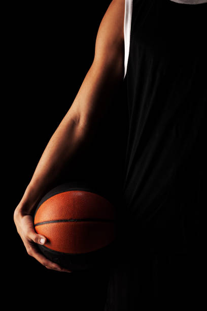 Professional basketball player holding a ball against black background. Serious concentrated african american man in sports uniform stock photo