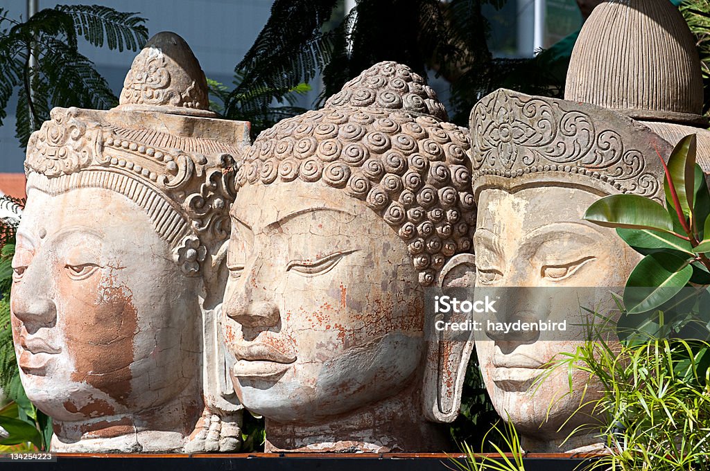 Três cabeças de Buda de pedra de sentar-se ao lado umas das outras, entre árvores - Foto de stock de Estátua royalty-free
