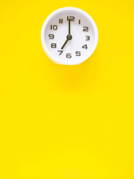 Top view, Flat lay, white clock showtime at 7 o'clock on office yellow workplace tabletop. Copy space for your text. Business and education concept. Vertical image