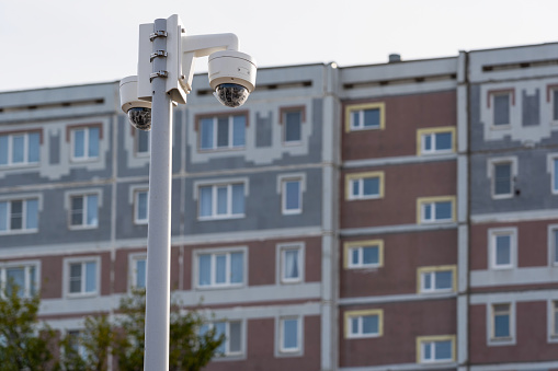 CCTV cameras on a pole, the facade of a panel apartment building in the background