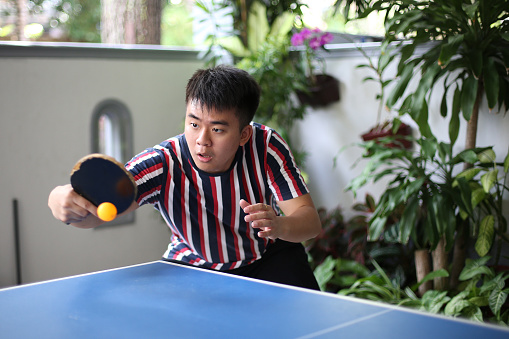An Asian young man is playing table tennis (ping pong) during leisure time.