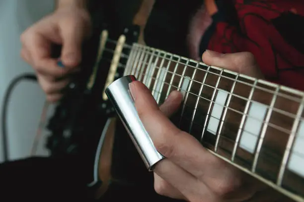 Person sliding a bottle neck along the strings of an electric guitar. Selective focus. Copy space.