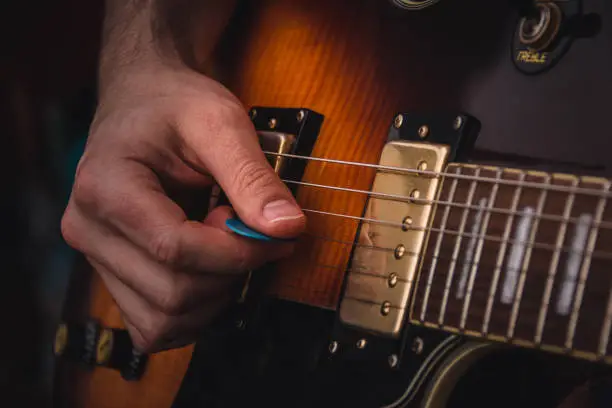 Person plucking the strings of an electric guitar with a pick. Selective focus. Copy space.