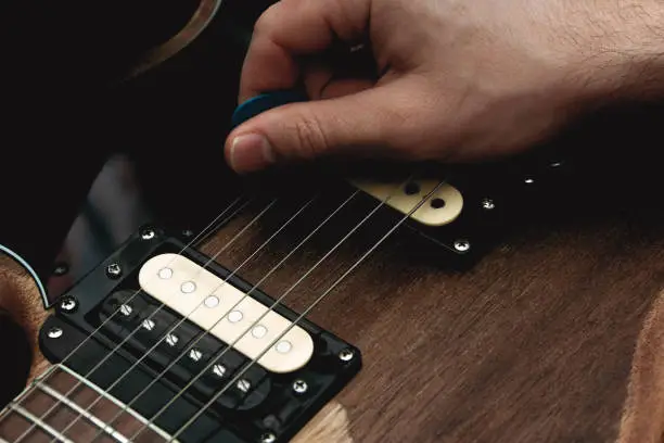 Person plucking the strings of an electric guitar with a pick. Selective focus. Copy space.
