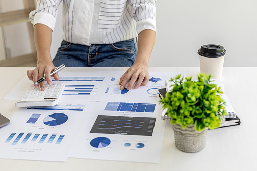 financial business woman pressing a white calculator, she uses a calculator to calculate the numbers in the company's financial documents that employees in the department create as meeting documents.