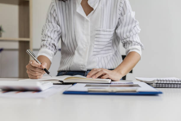 istock Business woman is taking notes in a notebook, she is checking sales documents and financial documents in her private office, she is the executive of a startup company. Business administration concept. 1342625964