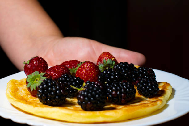 istock A white plate with a pancake with strawberries and blackberries, held by a woman's hand on a dark background. 1342626553