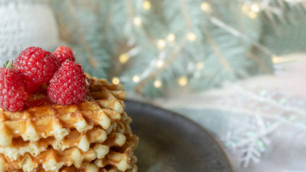 istock Viennese waffles with raspberries and honey on the Christmas table with tree branches and garlands of lights in the background. close-up, copy space 1342627540