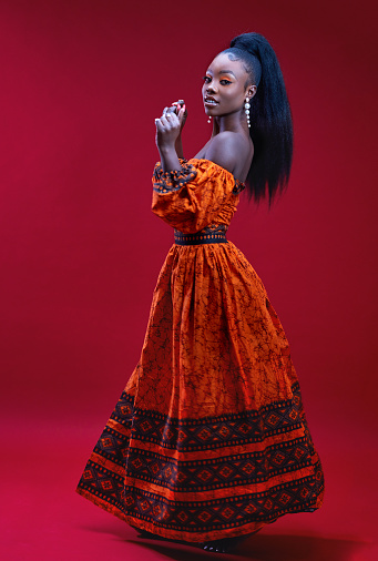 beautiful glamorous african woman in traditional dress dancing on red background, studio shot