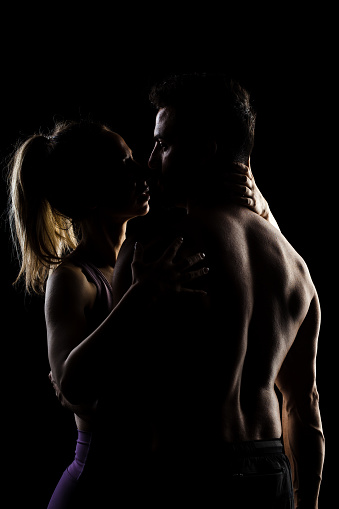 Fit couple posing together. Boy and girl side lit silhouettes on black background.