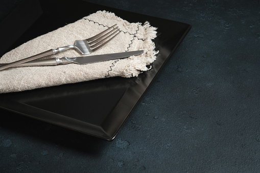 Cutlery and linen napkin on a square black platter. Table setting