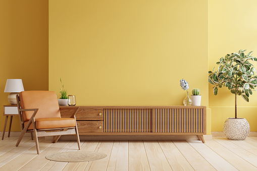 Gabinete tv en sala de estar moderna con sillón de cuero y planta sobre fondo de pared amarillo. photo