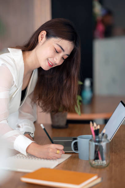 istock Young beautiful asian woman standing in office and writing note on the table. 1342704768