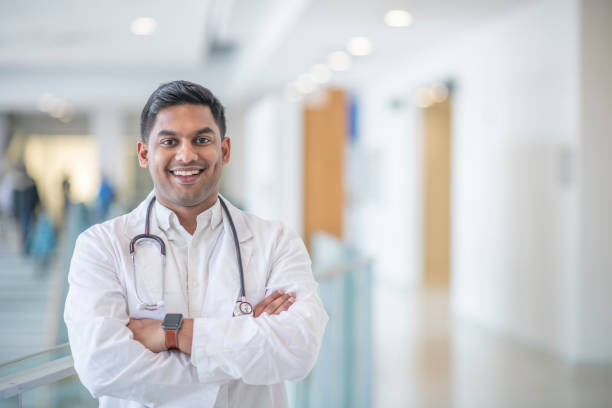 Portrait of a Male Doctor A male doctor of Indian decent, smiles in this medical portrait. His arms are crossed as he stands in a hallway.. doctor lifestyle stock pictures, royalty-free photos & images