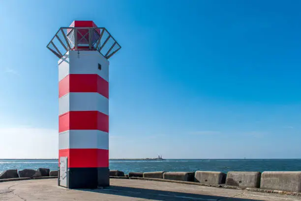 A red and white lighthouse at the end of the North pier marks the entry to the harbor of IJmuiden in The Netherlands