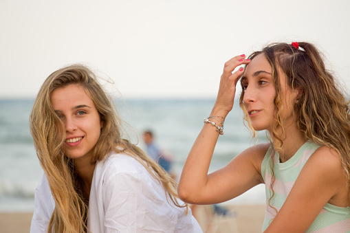 Young carefree female friends chilling on beach against sea while enjoying weekend in summer