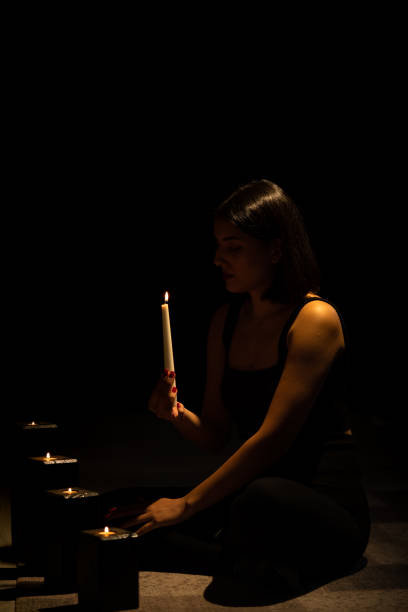 Portrait of mystical looking beautiful woman holding burning candle in hand in darkness with cinematic lighting. stock photo