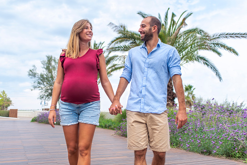 young happy couple in love of a pregnant woman and her boyfriend walking on the street having fun on holidays. quality family time holding hands on vacation days. joy, big belly and lifestyle concept