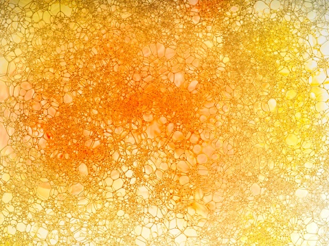 Yellow and orange soap soap bubble closeup. A colorful macro abstract of bubbles in translucent pan with strong backlighting. A textured background using various soluble pigments useful in various designs.